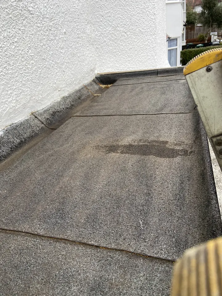 Before renewal: the existing flat-roof covering beside a white wall in Golders Green